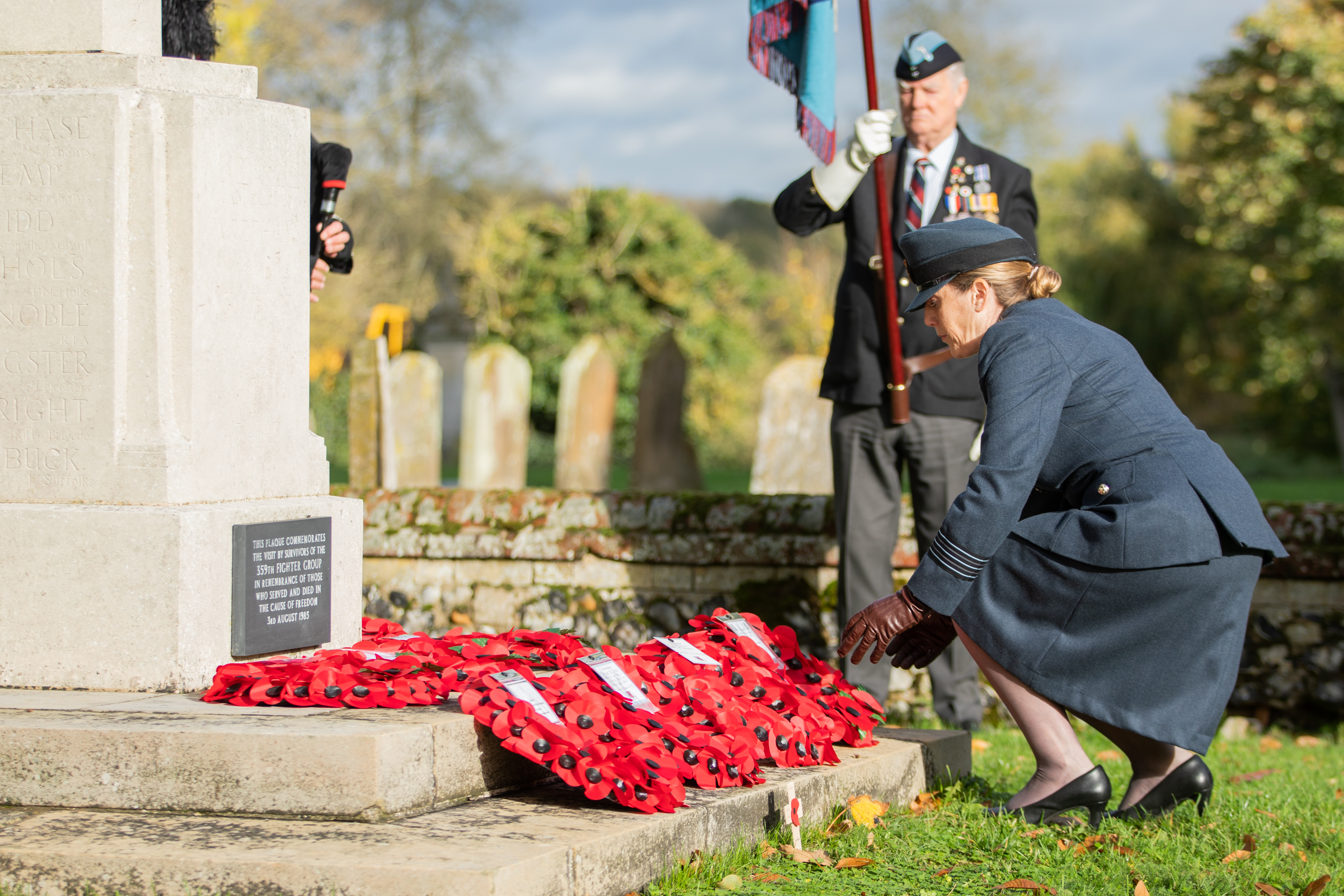 Image shows RAF aviator laying a poppy wreath by a memorial.